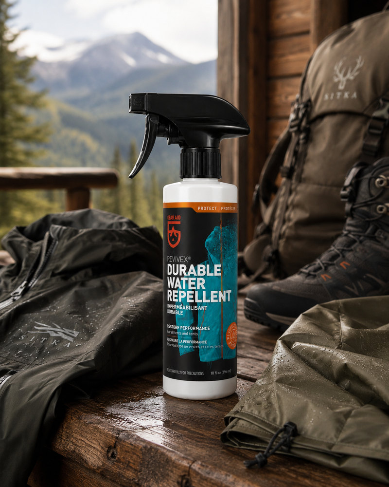 Load image into Gallery viewer, A bottle of Surver Durable Water Repellent outdoor gear spray stands on a wooden table in a mountain cabin setting, surrounded by hiking boots, jackets, and a backpack.