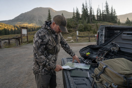Archery elk hunter reviews a license, hunting regulations and unit map on a truck tailgate at a Colorado mountain trailhead.