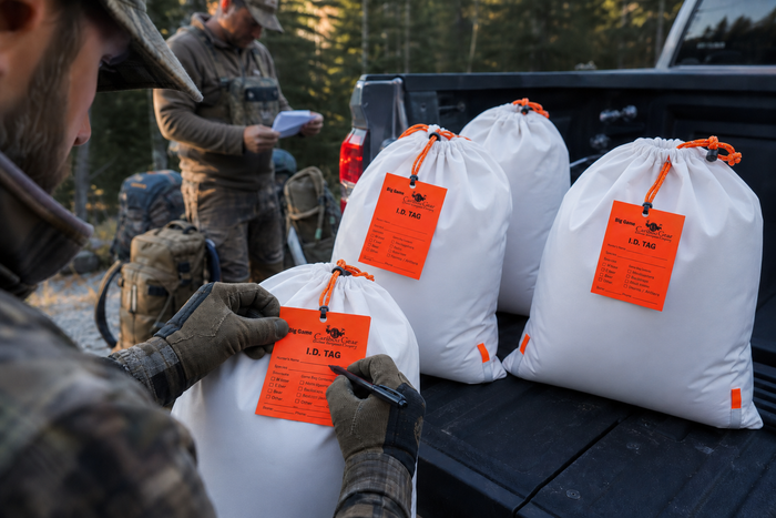 Western hunters label white Caribou Gear game bags with fluorescent-orange ID tags on a truck tailgate during a multi-hunter packout.