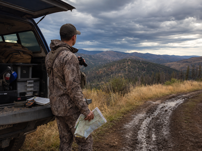 Western hunter watching afternoon storm clouds build over mountain terrain during summer scouting