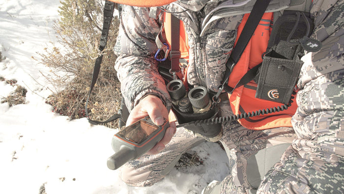 Hunter planning entry and exit route on a map with organized pack system and rifle protected during travel