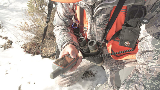 Hunter planning entry and exit route on a map with organized pack system and rifle protected during travel