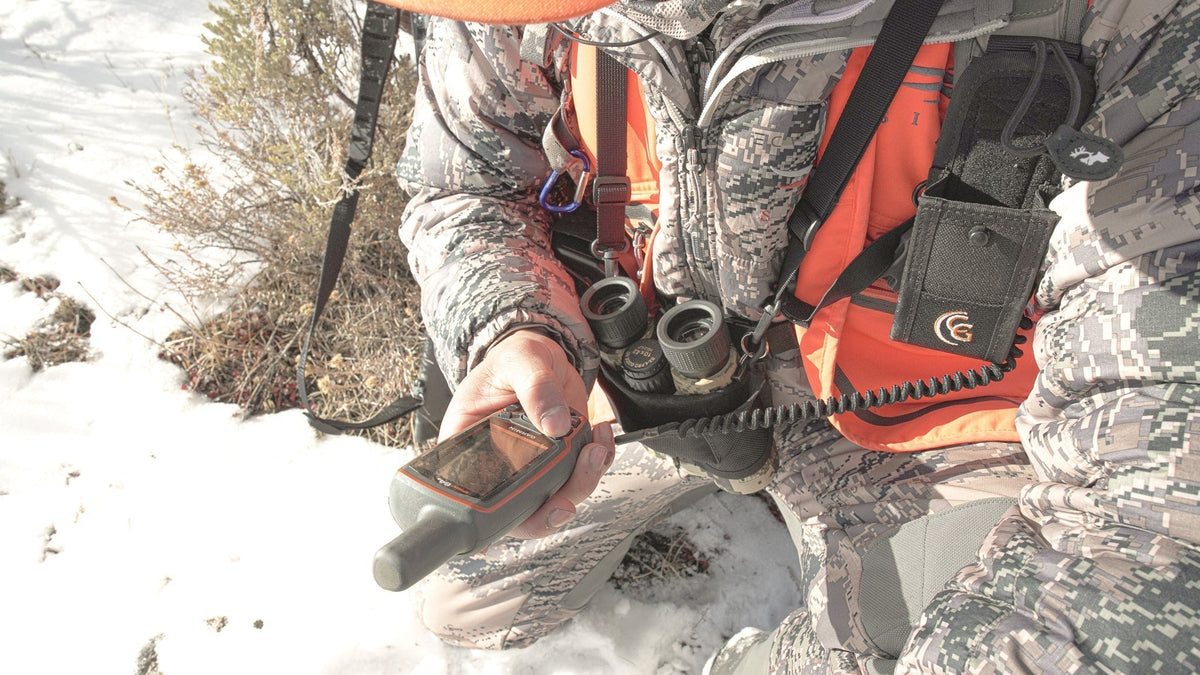 Hunter planning entry and exit route on a map with organized pack system and rifle protected during travel