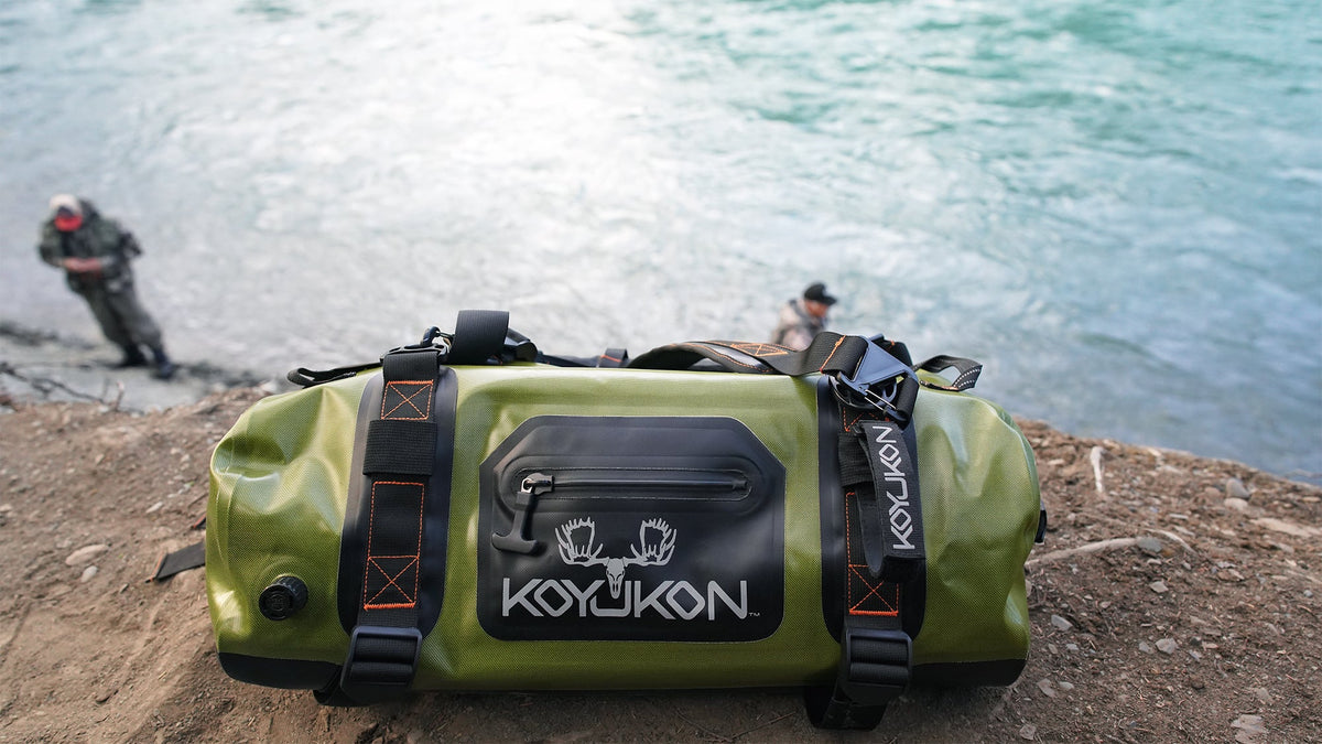Waterproof gray duffel and clear roll-top dry bag organized on a covered hunting-camp bench after rain.