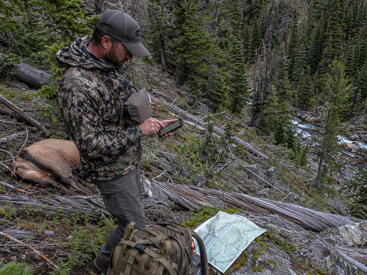 Hunter marking an elk kill site and packout route on a GPS while reviewing terrain in steep mountain country