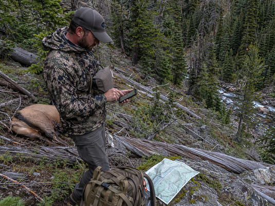 Hunter marking an elk kill site and packout route on a GPS while reviewing terrain in steep mountain country