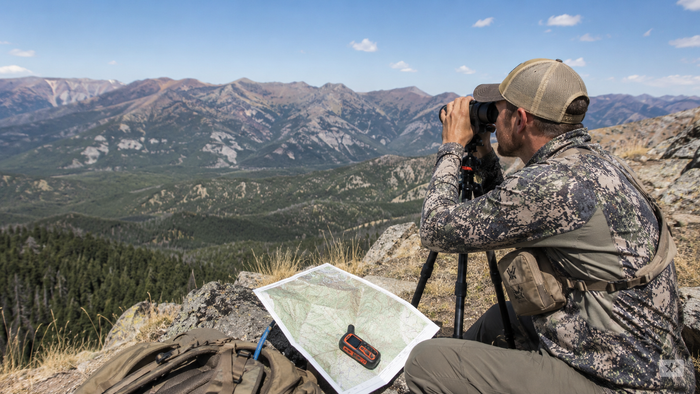Western hunter glassing elk country during summer scouting while reviewing maps and terrain