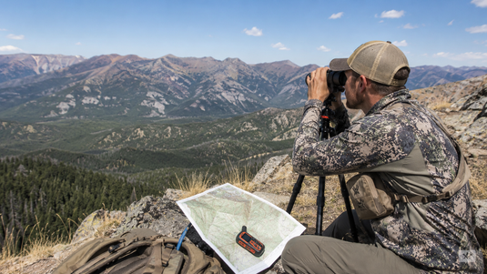 Western hunter glassing elk country during summer scouting while reviewing maps and terrain