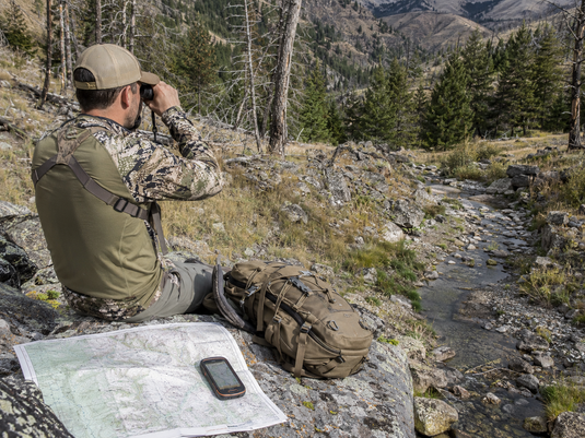 Western hunter glassing near a mountain water source while evaluating summer conditions before elk season