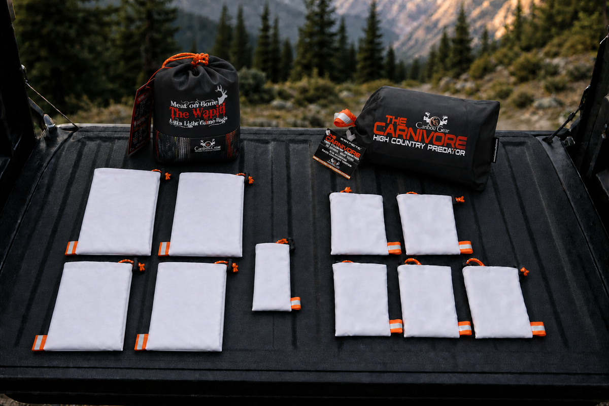 Wapiti and Carnivore elk game bag systems arranged with their branded storage packages on a truck tailgate at a mountain trailhead.